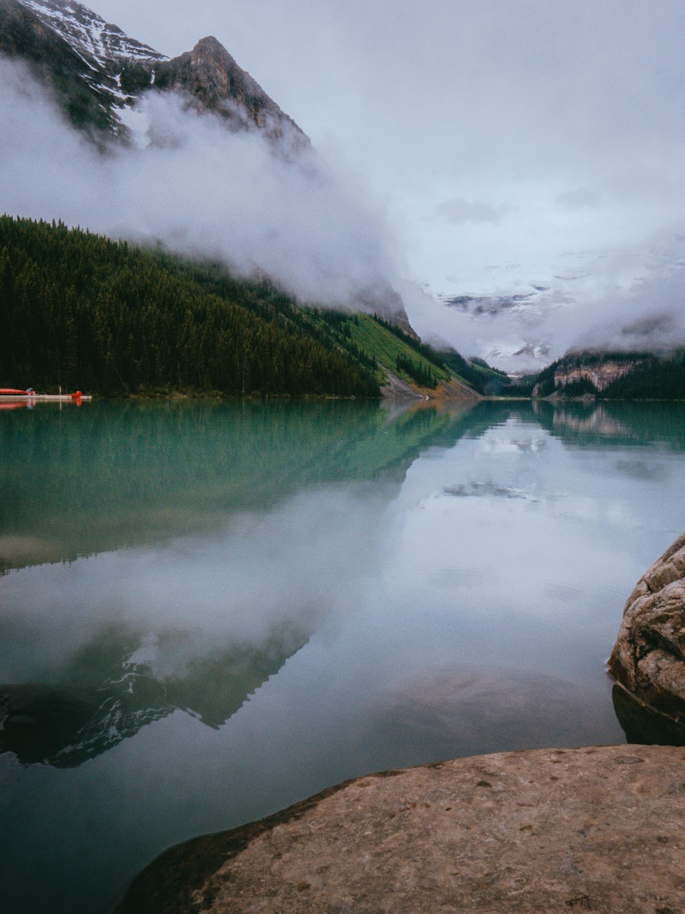 lake near green trees under white clouds during daytime