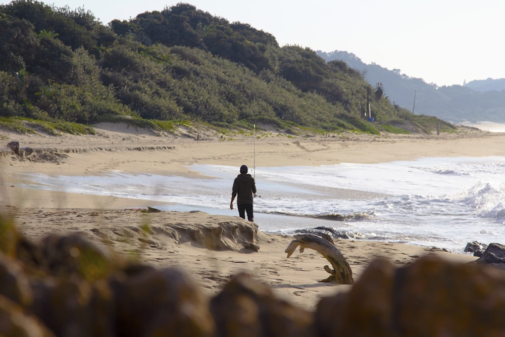 Hombre con chaqueta negra caminando en la playa durante el día