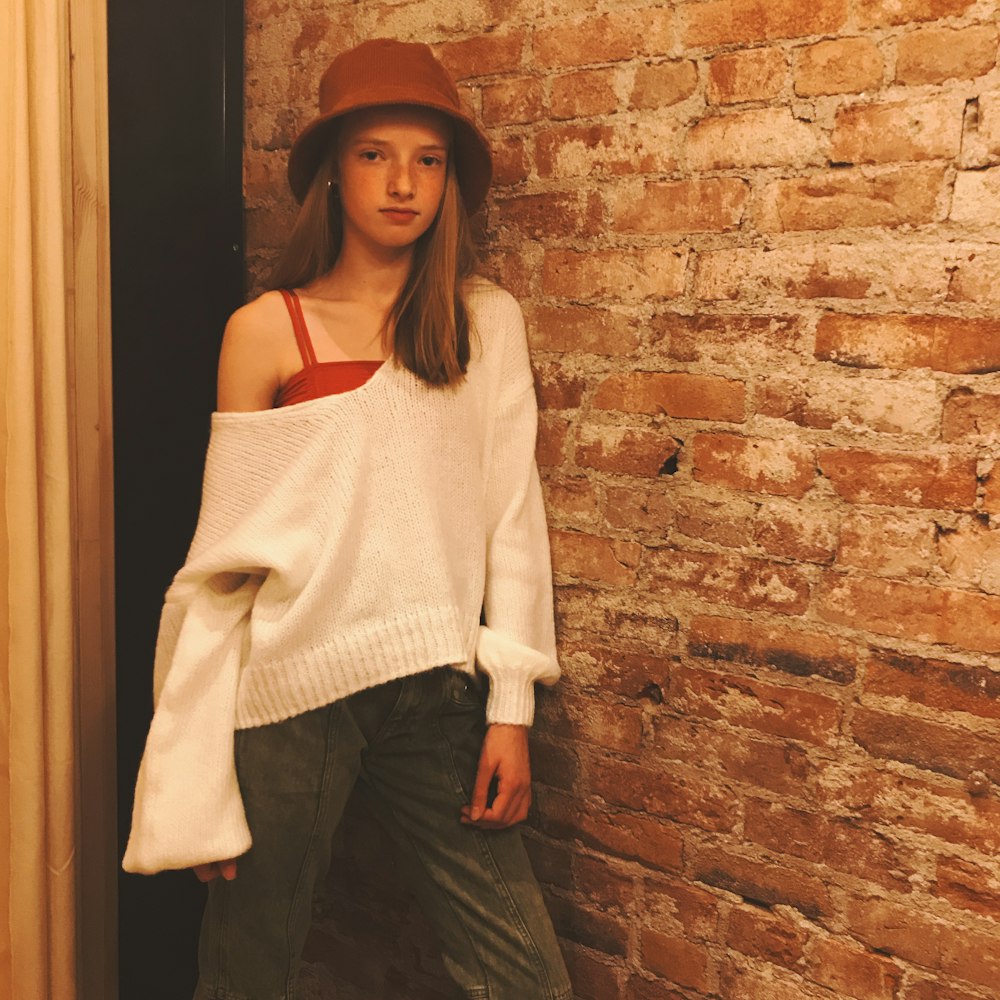 woman in white knit sweater and black skirt standing beside brick wall