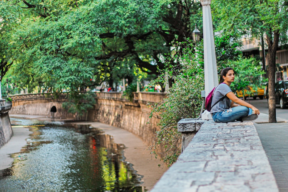 man in blue shirt sitting on concrete bench near river during daytime