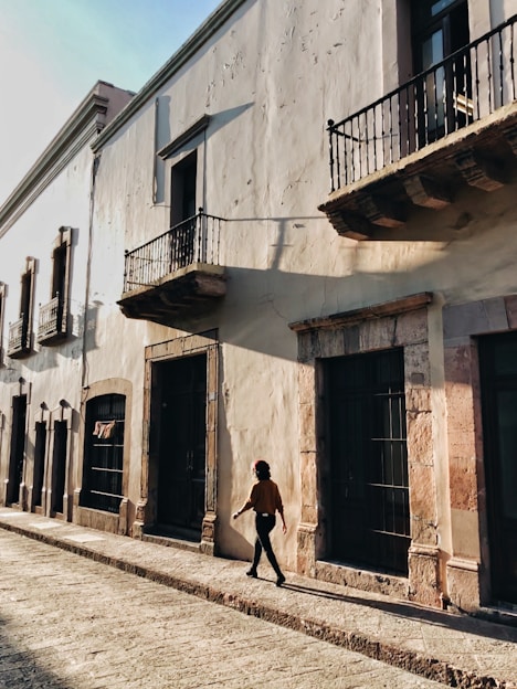 A traveler walking along a sunlit cobblestone street lined with colorful buildings and local shops.