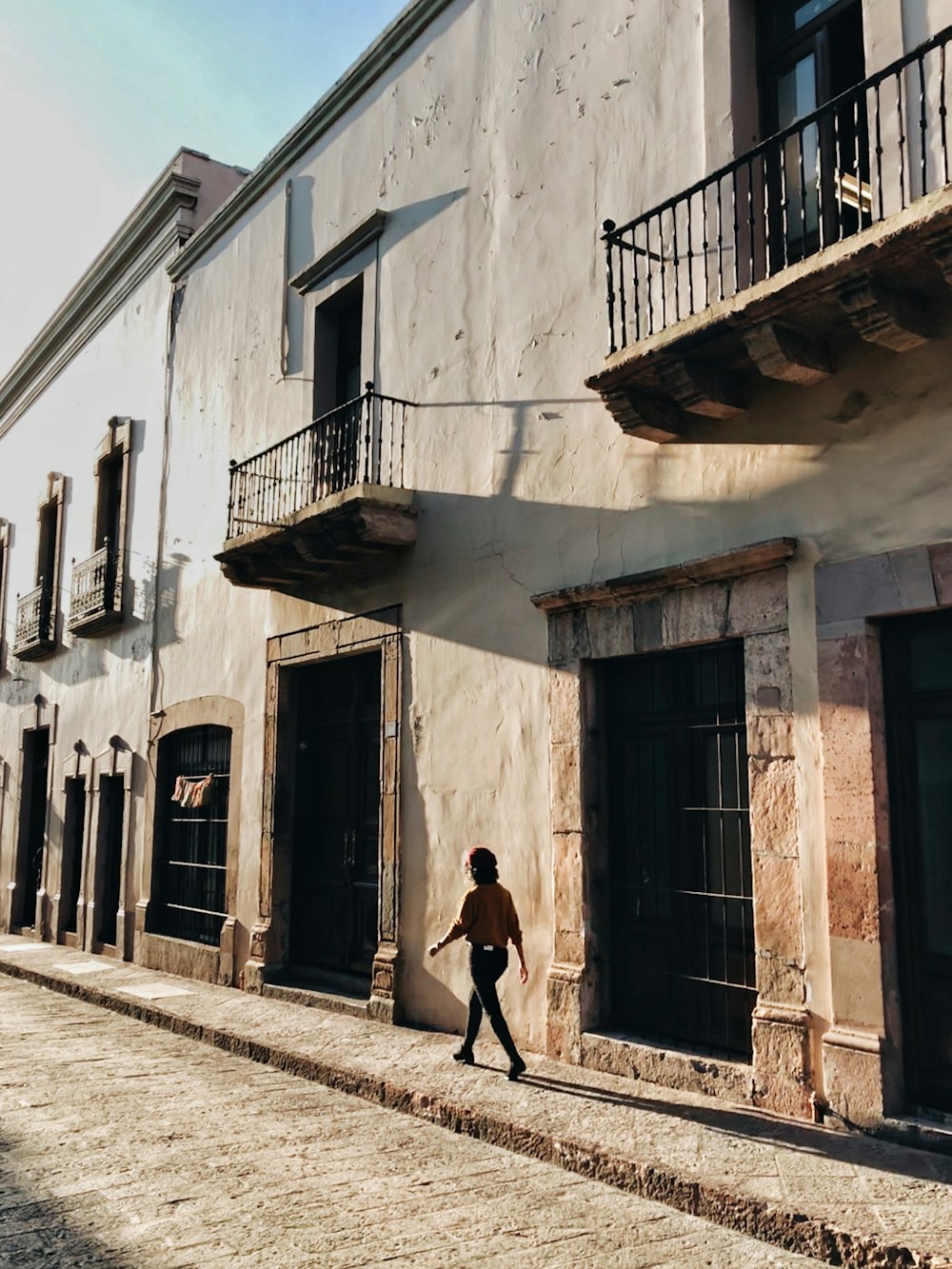 Hombre con camiseta negra y pantalones negros caminando por la acera durante el día