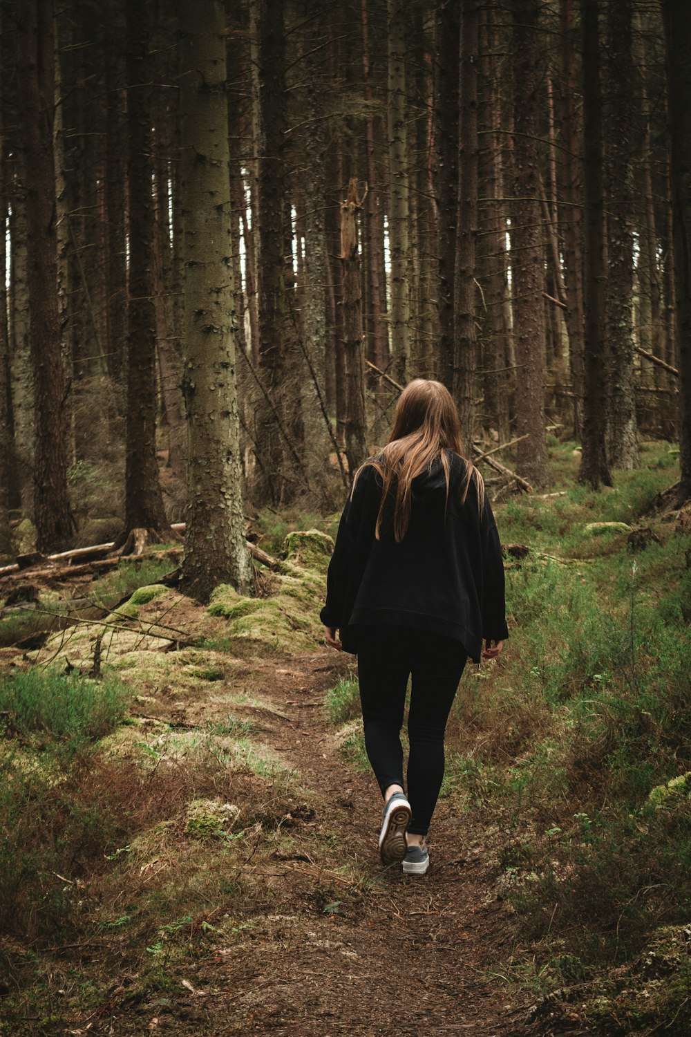 woman in black coat walking on forest during daytime