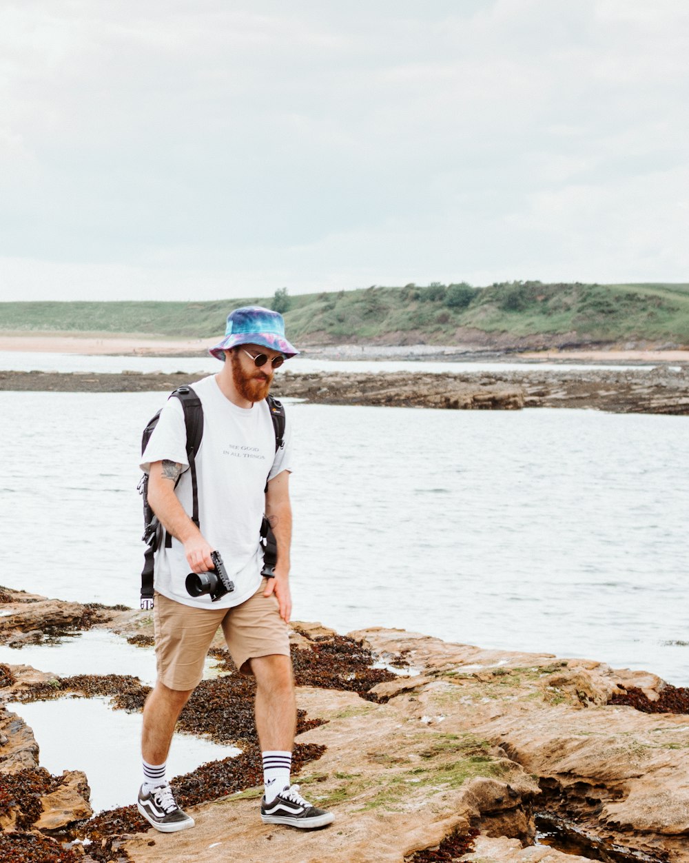 man in white shirt and brown shorts standing on brown rock near body of water during