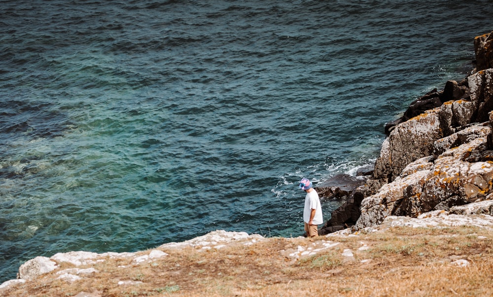 woman in white shirt standing on rock near body of water during daytime