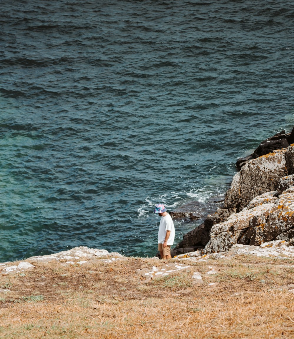 woman in white shirt and pink pants standing on brown rock near body of water during