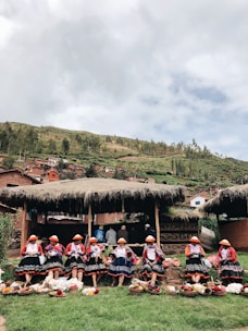 A group of indigenous women teaching children traditional Andean crafts outdoors.