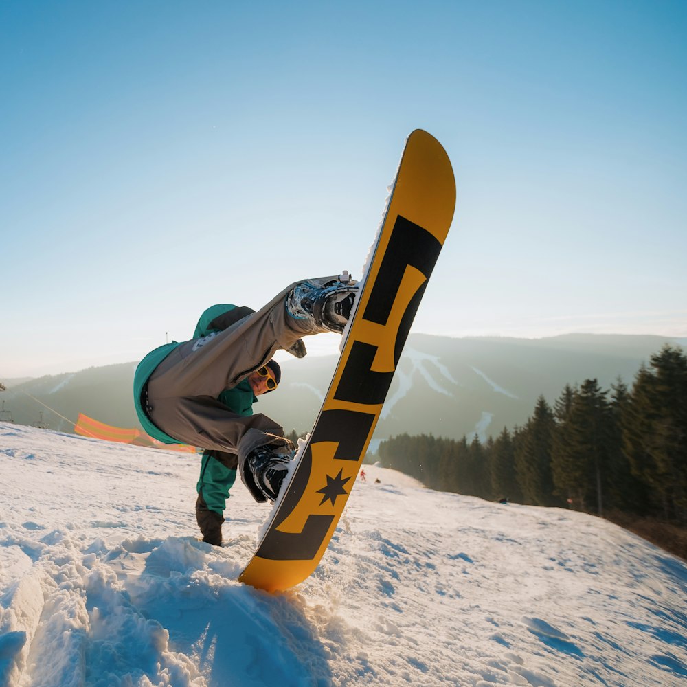 man in black jacket and yellow pants riding yellow snowboard on snow covered ground during daytime