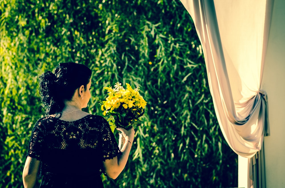 woman in black floral dress holding yellow flower bouquet