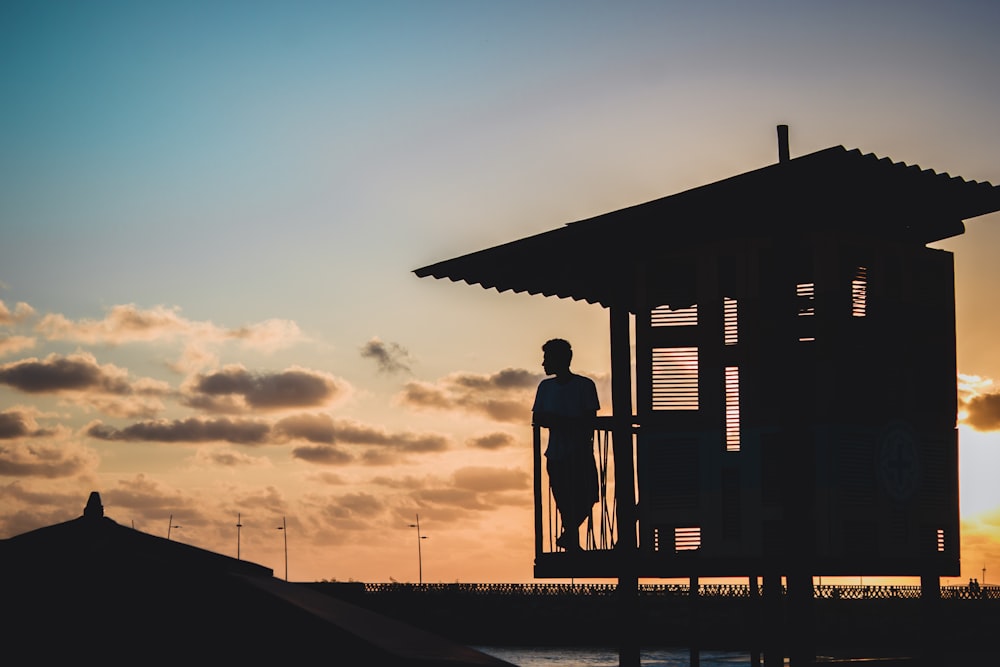 Silueta del hombre de pie en el muelle de madera durante la puesta del sol