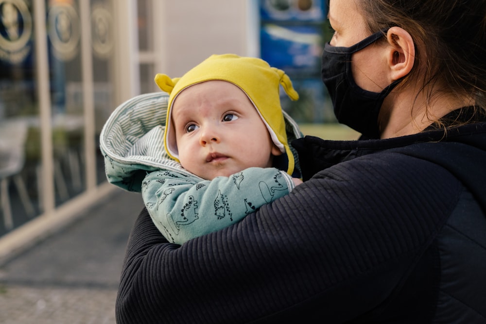 woman in black long sleeve shirt carrying baby in yellow knit cap