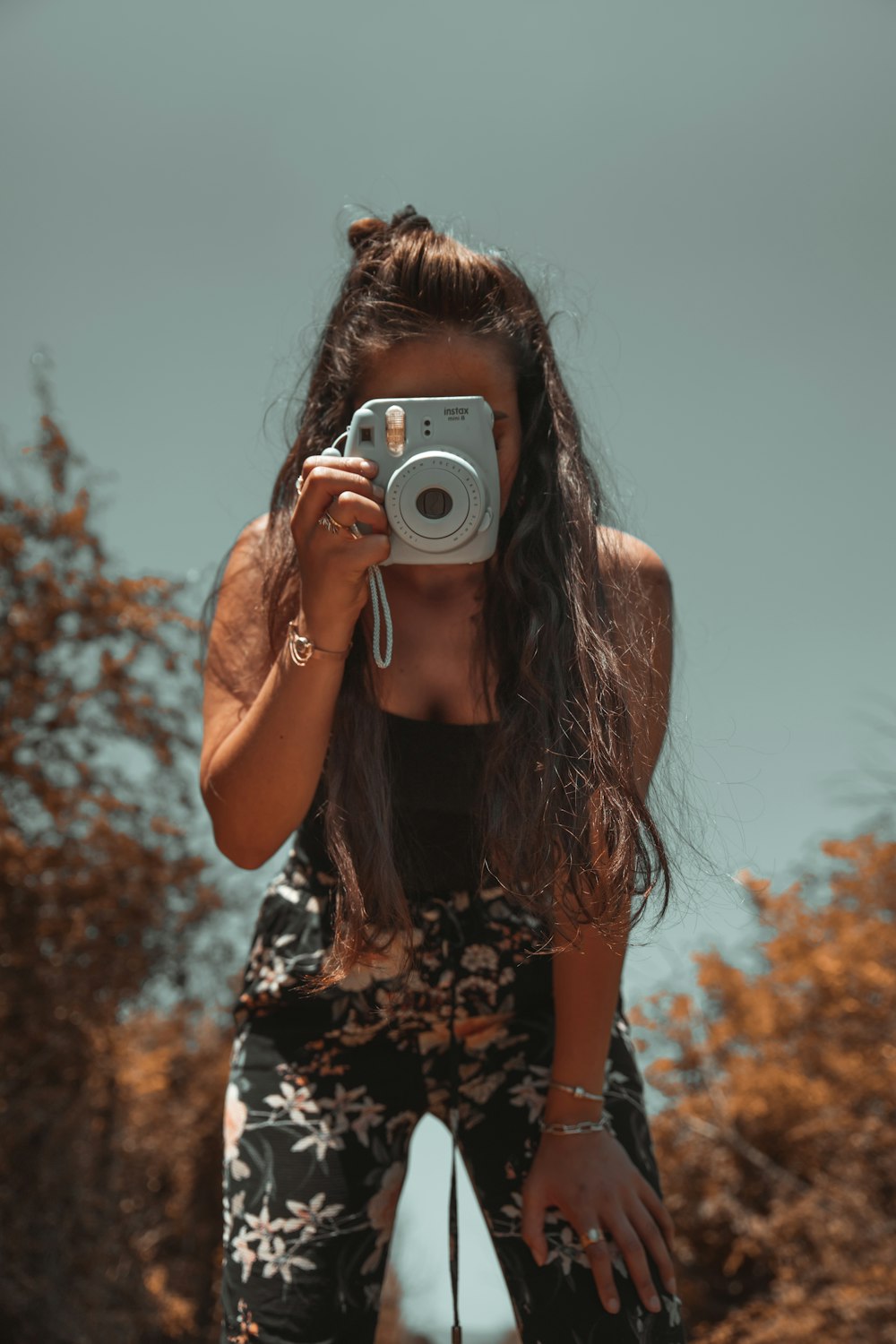 woman in black and white floral tank top holding gray point and shoot camera