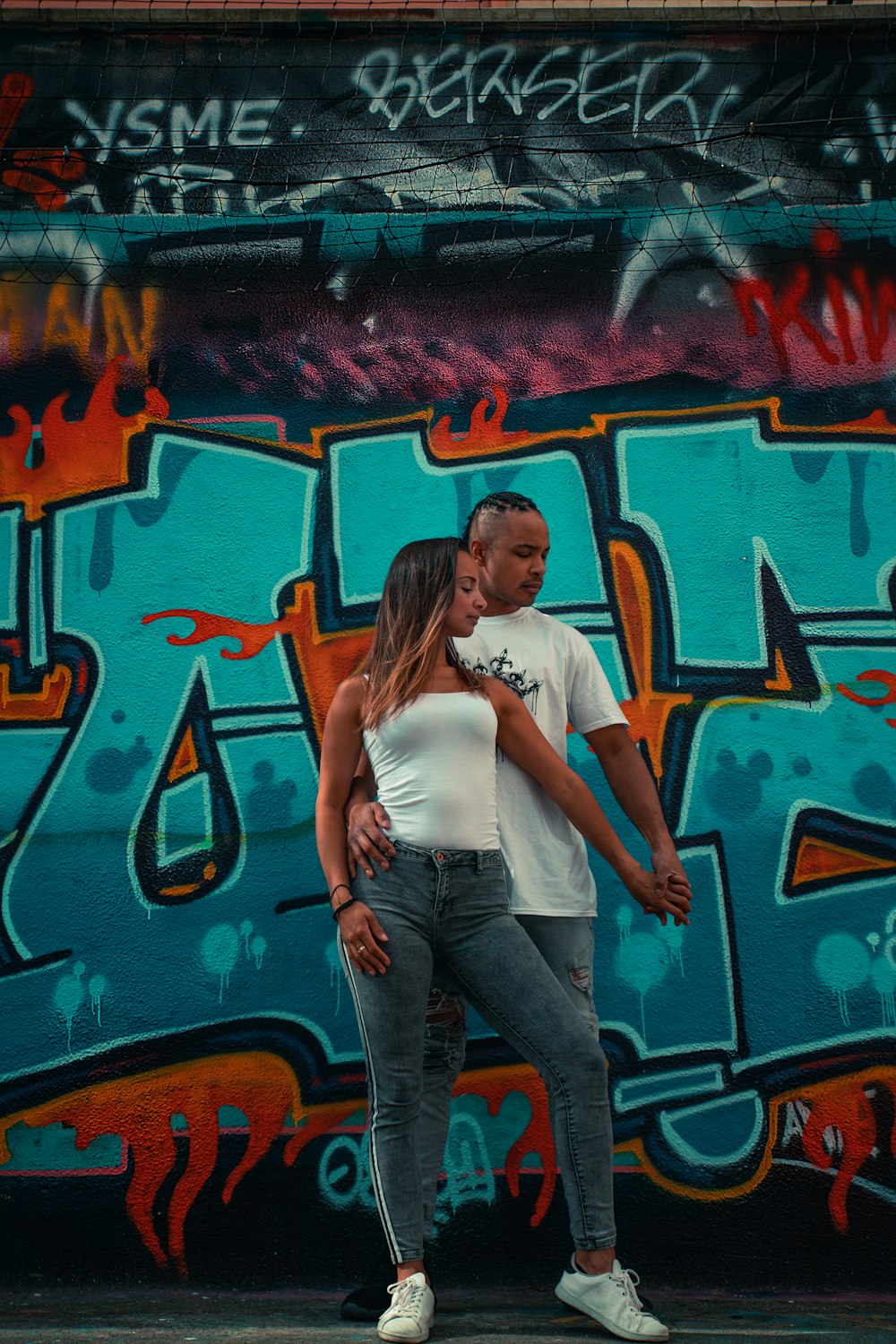 woman in white shirt and blue denim jeans standing beside graffiti wall