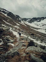A rugged mountain range with dramatic shadows and a small group hiking along a narrow trail.
