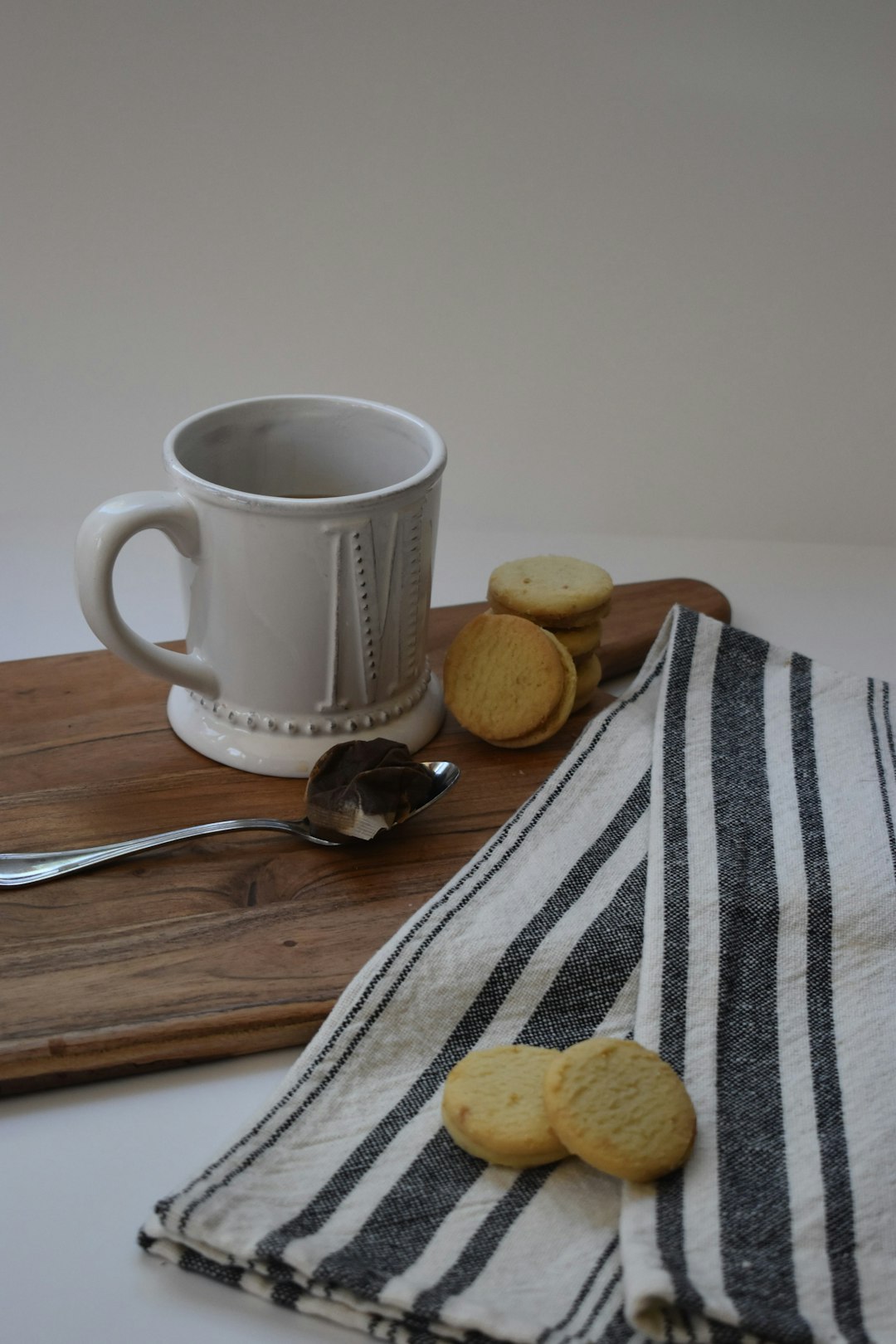 white and black checkered ceramic mug beside stainless steel spoon on brown wooden table