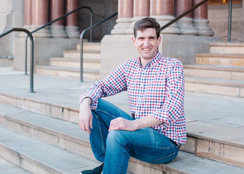 man in blue and white checkered dress shirt and blue denim jeans sitting on concrete stairs