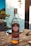 A bottle of Havana Club Añejo Especial Cuban rum is placed on a wooden outdoor table. The setting suggests a sunny day, with blurry background elements indicating an outdoor dining area. The label on the bottle features distinctive branding and blue and gold accents. Other objects, such as a utensil and a plate, are partially visible, emphasizing a casual and relaxed outdoor atmosphere.
