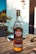 A bottle of Havana Club Añejo Especial Cuban rum is placed on a wooden outdoor table. The setting suggests a sunny day, with blurry background elements indicating an outdoor dining area. The label on the bottle features distinctive branding and blue and gold accents. Other objects, such as a utensil and a plate, are partially visible, emphasizing a casual and relaxed outdoor atmosphere.