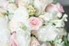 A close-up of a delicate bouquet featuring soft pink roses and white lilies wrapped in rustic paper.