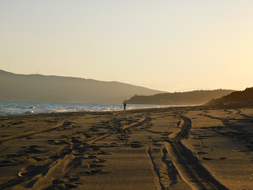 Persona parada en arena marrón cerca del cuerpo de agua durante el día