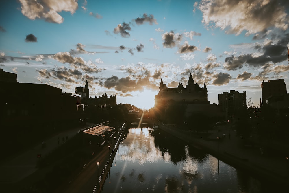 silhouette of buildings near body of water under blue sky and white clouds during daytime