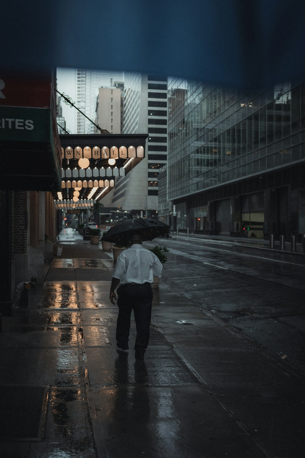 person in black jacket and black pants holding umbrella walking on sidewalk during night time