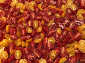 A vibrant assortment of sliced cherry tomatoes is displayed, featuring a mix of red and yellow varieties. The tomatoes are juicy and fresh, with visible seeds and a glossy texture.