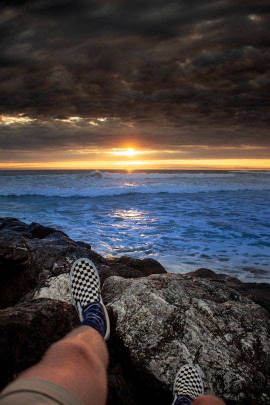 person in black and white checkered pants sitting on rock near sea during sunset in Mimizan Plage France