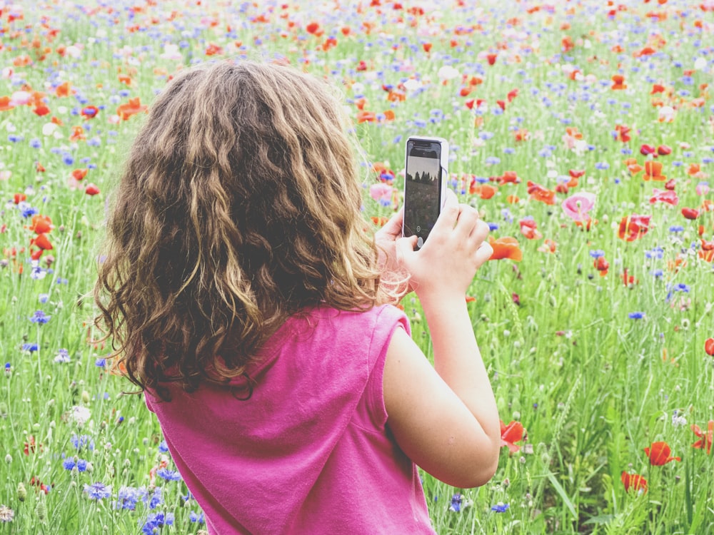 girl in pink shirt taking photo of pink flowers