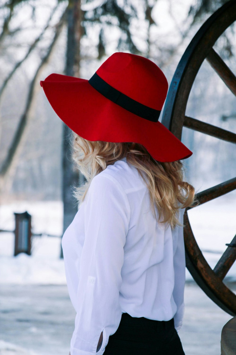 mulher na camisa branca da manga comprida que veste o chapéu vermelho em pé ao lado da roda de metal marrom durante o dia