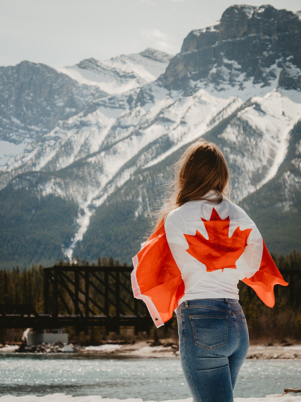 woman in white and red hoodie standing on brown wooden bridge during daytime