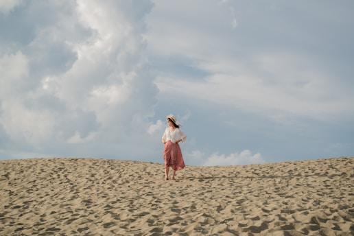 woman in white and red dress standing on brown sand under white clouds during daytime