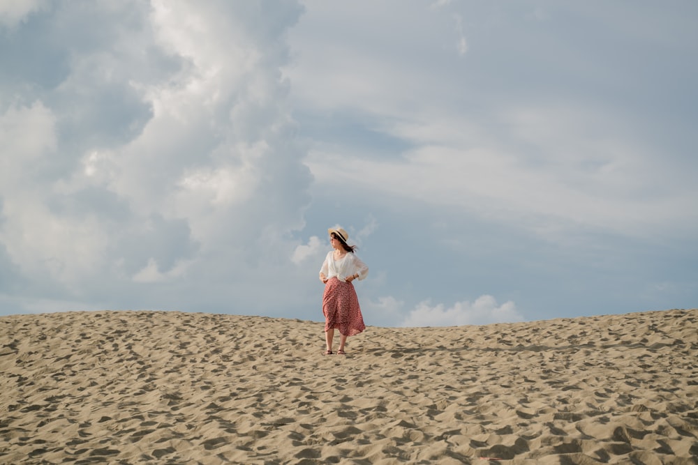 woman in white and red dress standing on brown sand under white clouds during daytime