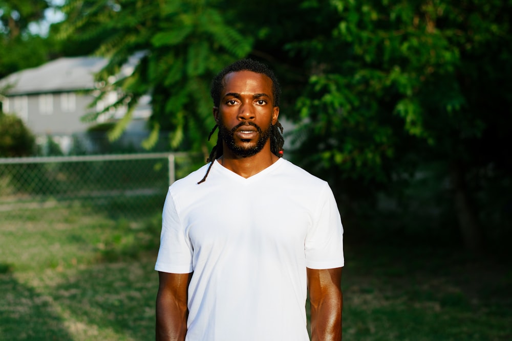 man in white polo shirt standing near green trees during daytime