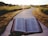 An open Bible held up against a backdrop of a winding path that leads through a grassy field, with the sun setting in the distance casting a warm glow over the scene.