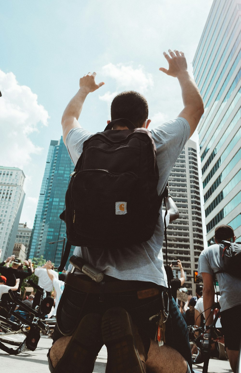 man in white shirt and black backpack raising his hands