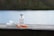 A vial of insulin and two syringes are placed on a wooden surface. The background features a blurred view of a lake and greenery, giving the scene a peaceful and serene outdoor setting.