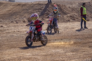 2 men riding motocross dirt bikes on brown field during daytime