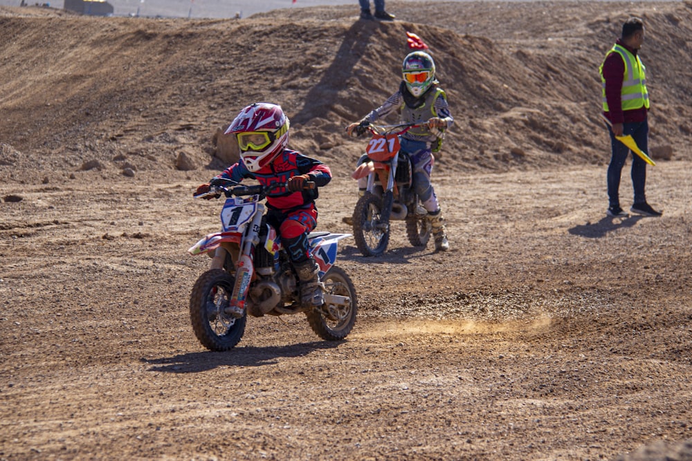 2 men riding motocross dirt bikes on brown field during daytime