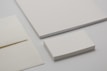 Various forms of blank stationery items are arranged, including a stack of business cards, an envelope, and sheets of paper, all placed on a neutral-colored surface.