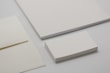 Various forms of blank stationery items are arranged, including a stack of business cards, an envelope, and sheets of paper, all placed on a neutral-colored surface.