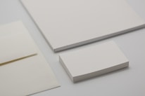 Various forms of blank stationery items are arranged, including a stack of business cards, an envelope, and sheets of paper, all placed on a neutral-colored surface.