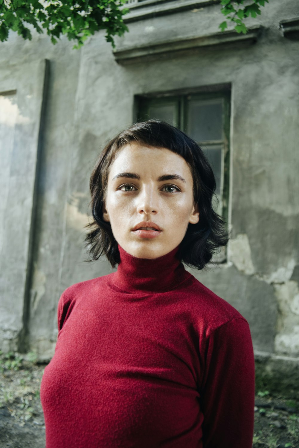 woman in red turtleneck sweater standing beside gray concrete wall