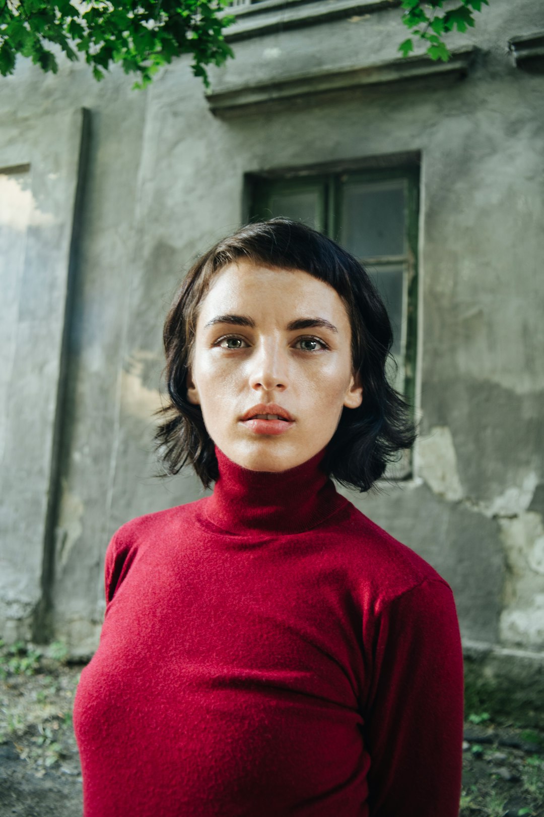 woman in red turtleneck sweater standing beside gray concrete wall