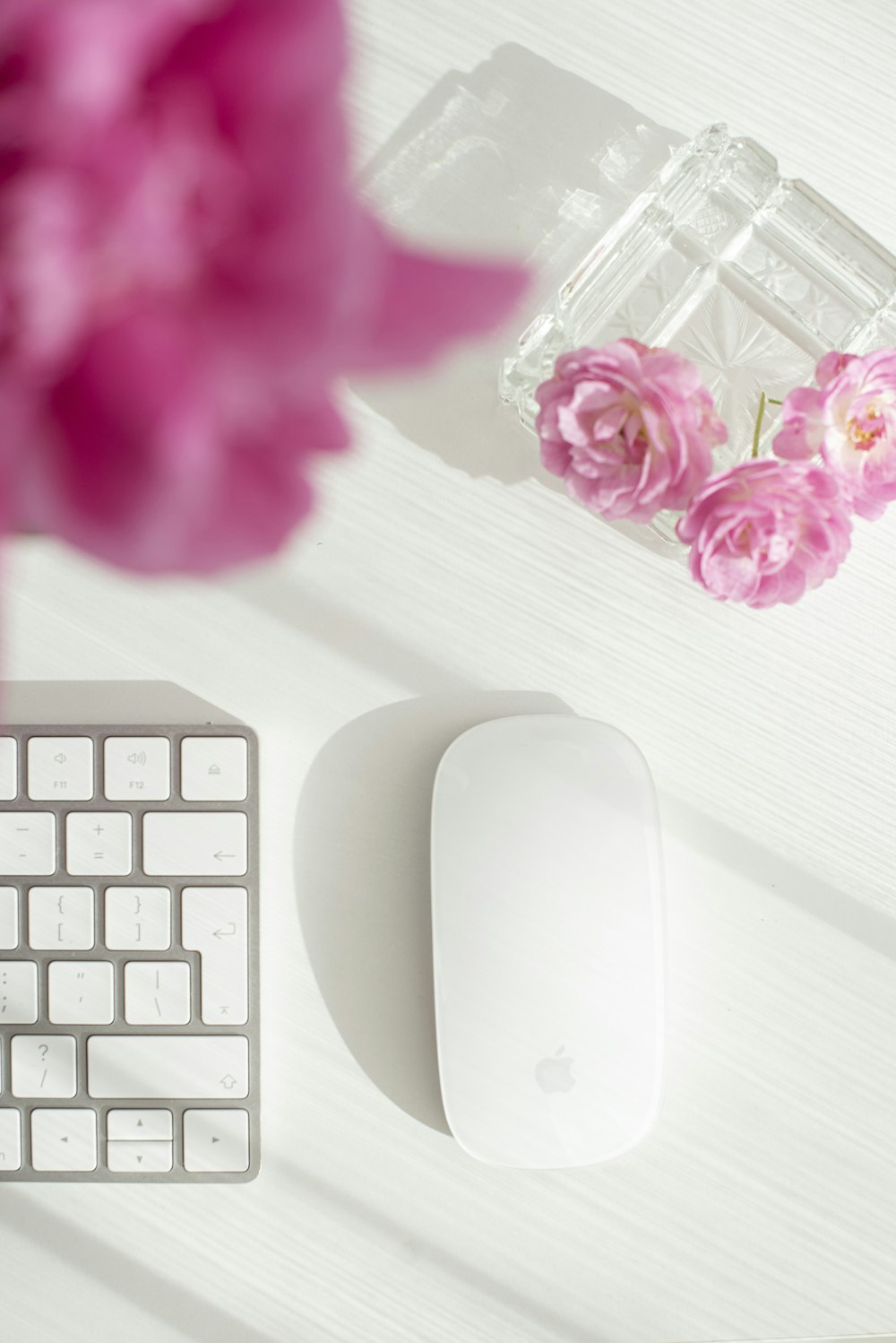 白い木製のテーブルの上のピンクの花の横の白いリンゴの魔法のマウス