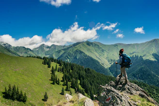 A hiker standing on a volcanic ridge overlooking lush green valleys under a vibrant sky.