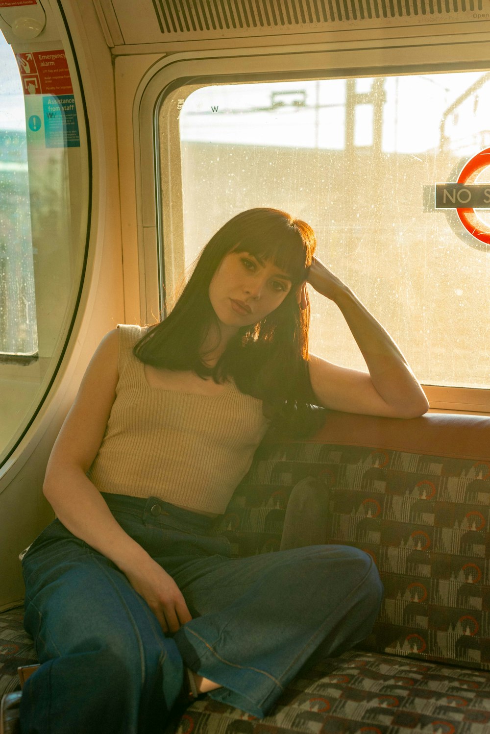 woman in beige tank top and blue denim jeans sitting on gray and brown chair