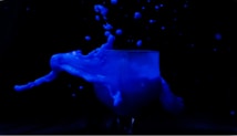 An elegant display of a blue liquid splashing out of a transparent glass, captured against a stark black background. The liquid forms dynamic shapes as droplets are suspended in the air, creating a sense of motion and fluidity.