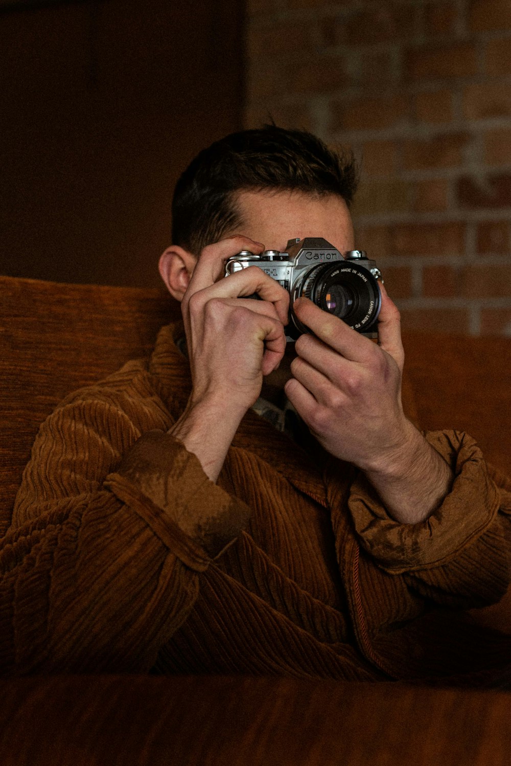 man in brown sweater holding black dslr camera