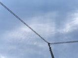 An overhead view of a utility pole with wires extending across a cloudy sky, indicating a network of power or communication lines.